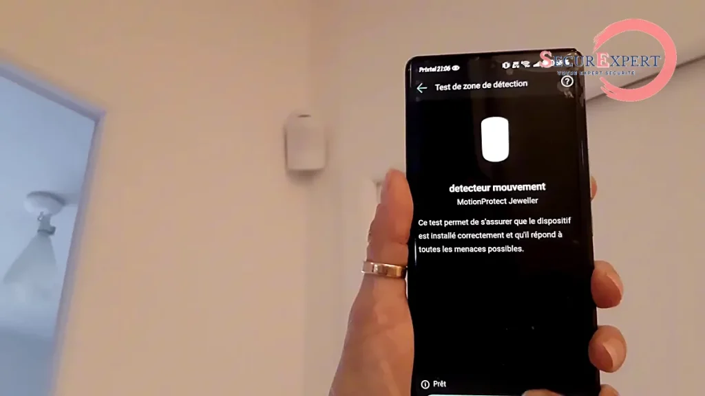 MotionProtect Ajax installé dans l’angle d’une pièce avec le test de zone de détection sur smartphone